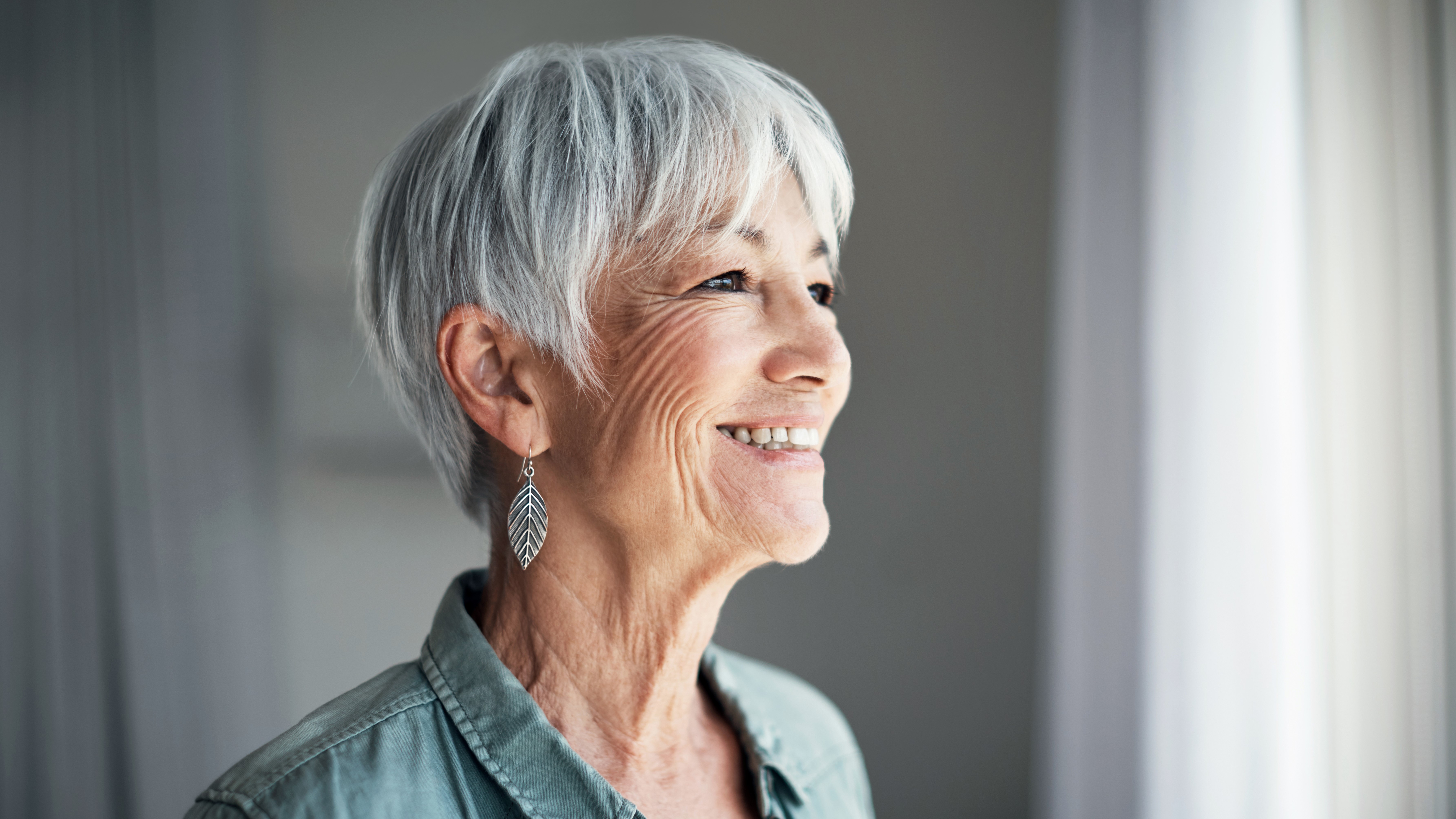 Frau mit grauen Haaren schaut glücklich in die Ferne.