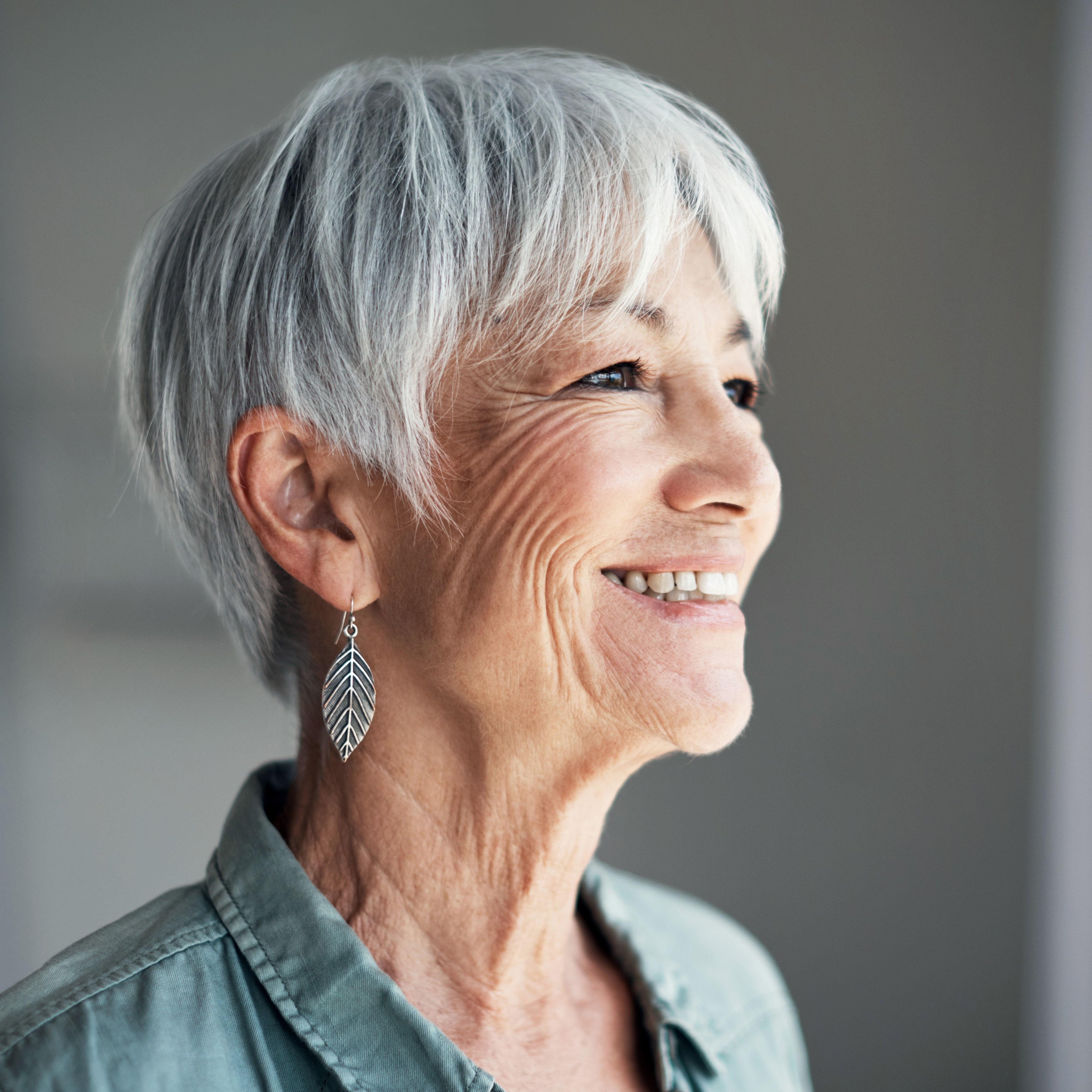 Frau mit grauen Haaren schaut glücklich in die Ferne.