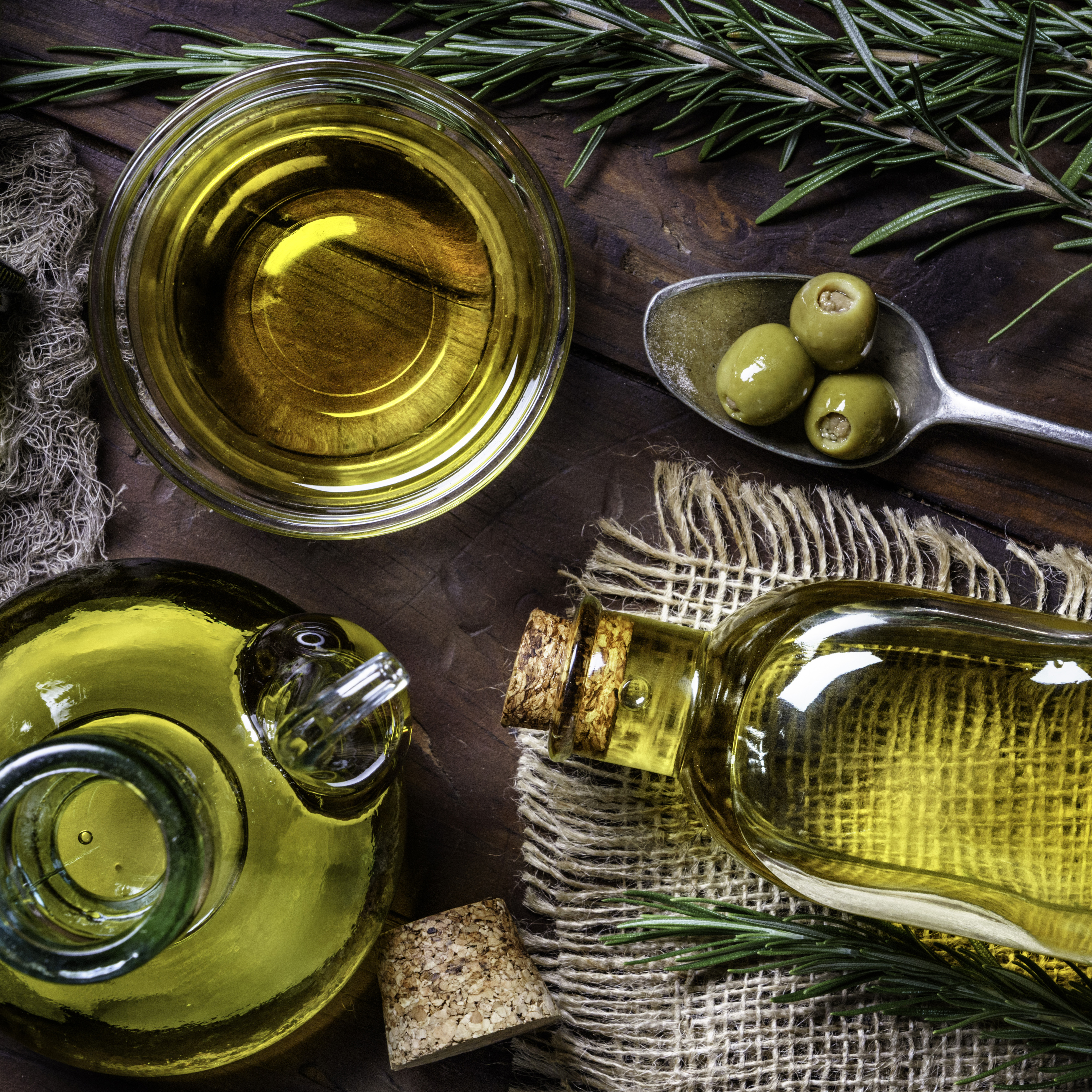 Eine Flasche Olivenöl neben Oliven auf Holzuntergrund