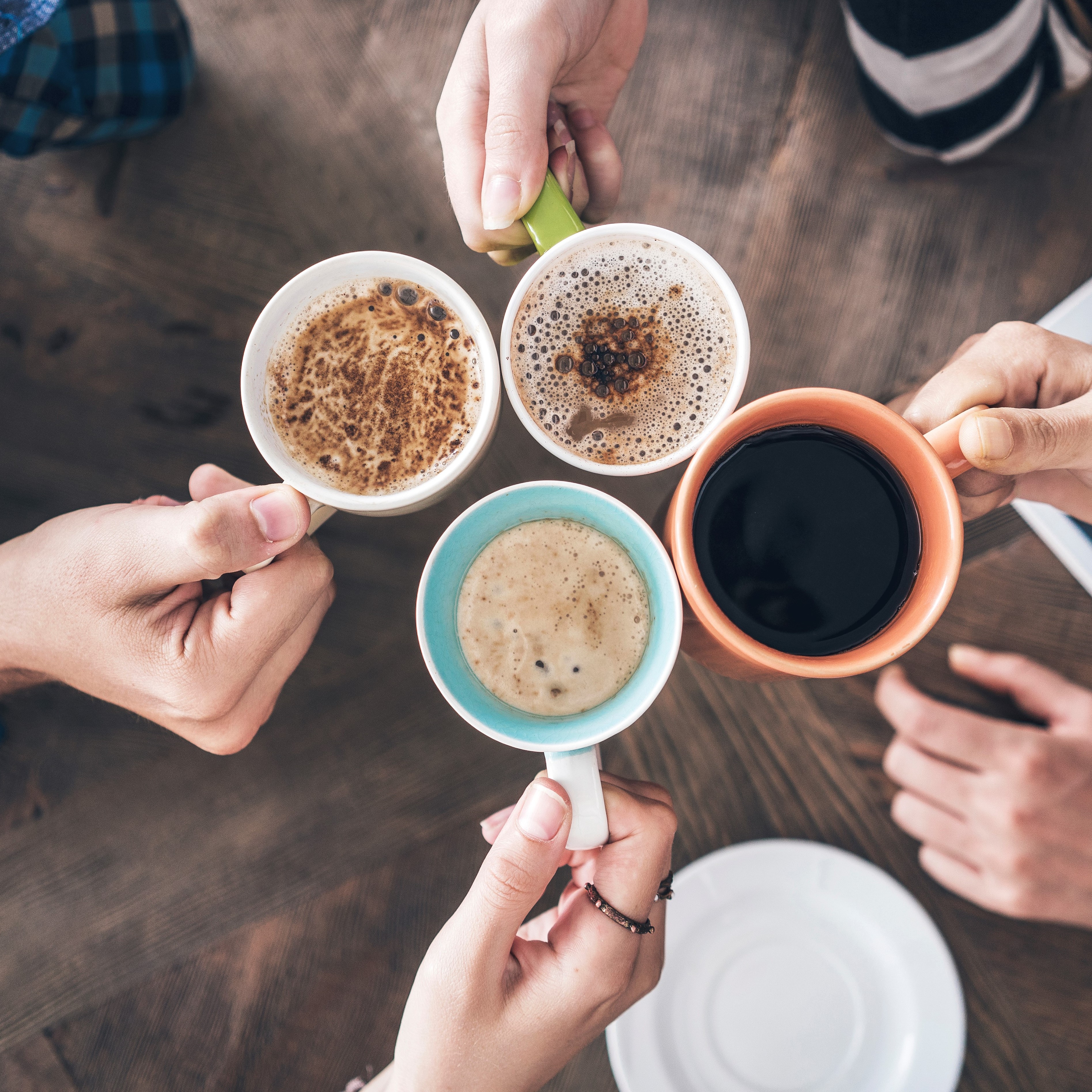 4 Menschen stoßen mit Kaffee über Bürotisch an.