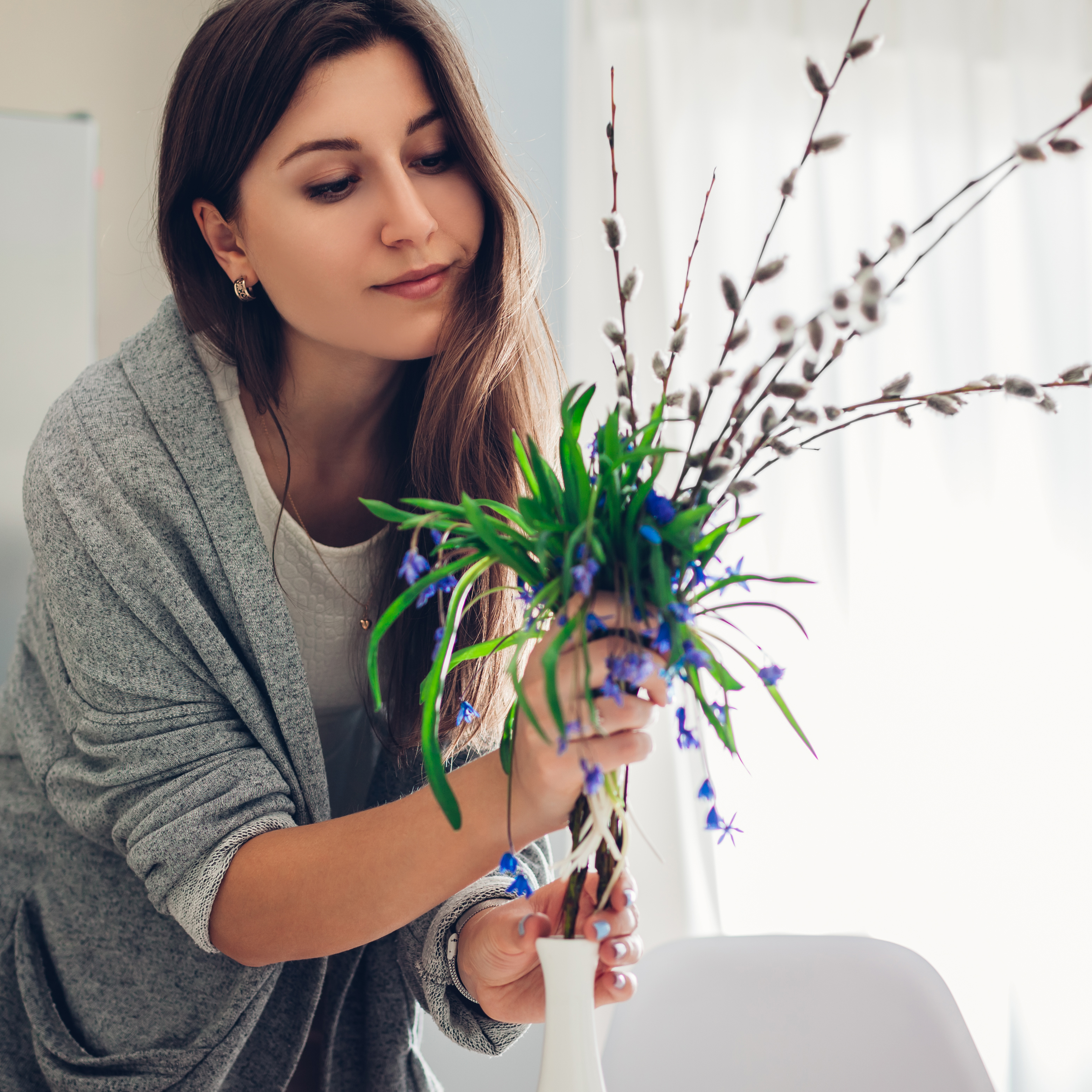 Eine Frau arrangiert Weidenkätzchen und Blumen in einer Vase. 